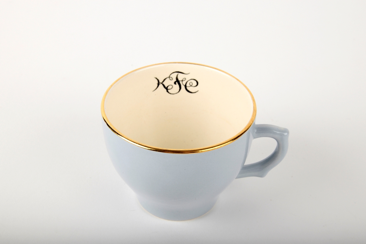Kaffekopp med fat.

Koppen har monogram på innsiden. Både koppen og fatet har gullfarget kant. Fatet er hvitt i midten.