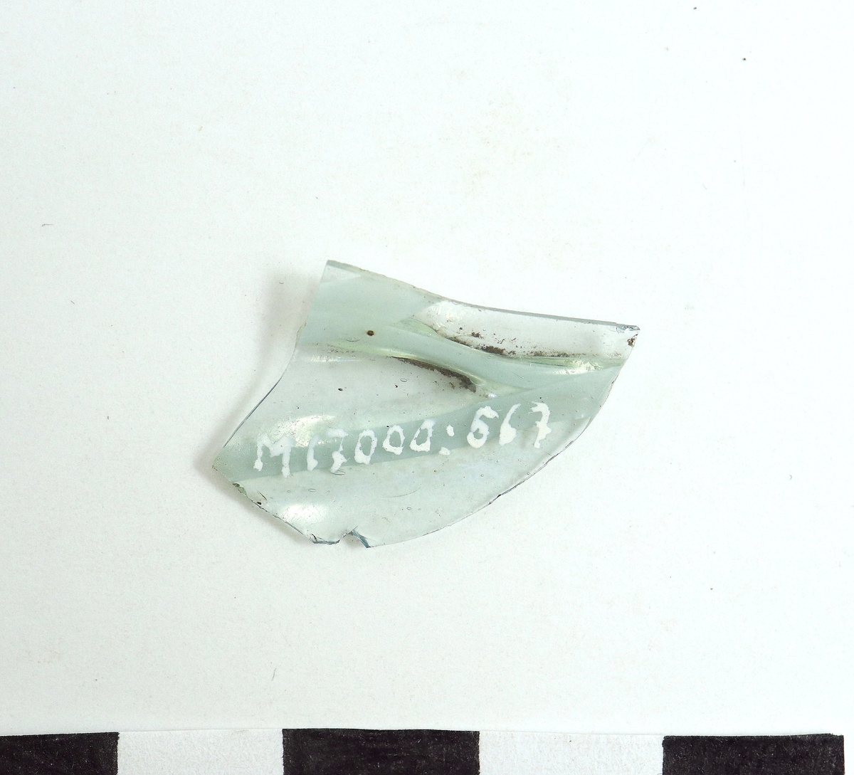 Ett ornerat venetianskt glas i svagt blå färg. På glaset finns två skikt pålagda vita trådar, (vetro a fili) i relief. Troligen samma eller liknande kärl som M 17000-565-566.