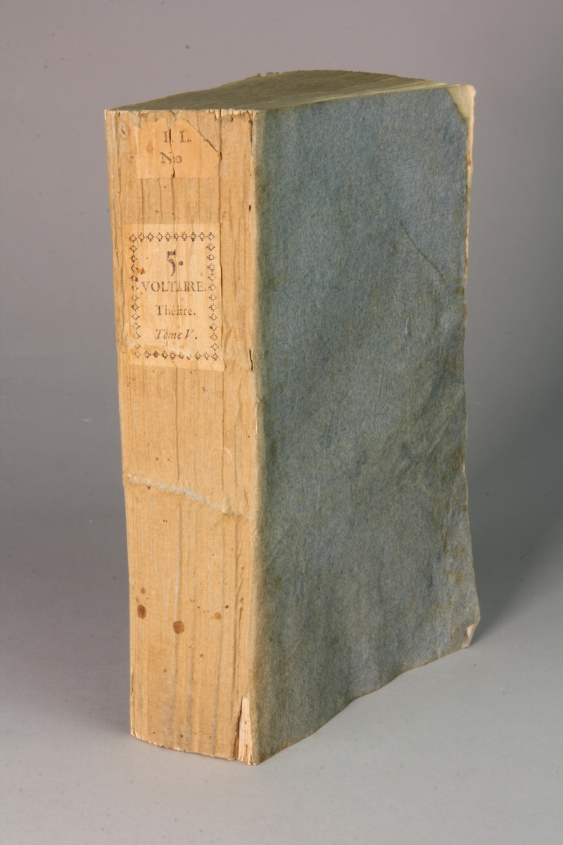 Bok, häftad,"Oeuvres complètes de Voltaire." del 5, tryckt 1785.
Pärm av gråblått papper, skurna snitt. På ryggen pappersetikett med tryckt text med volymens namn och nummer. Ryggen blekt.