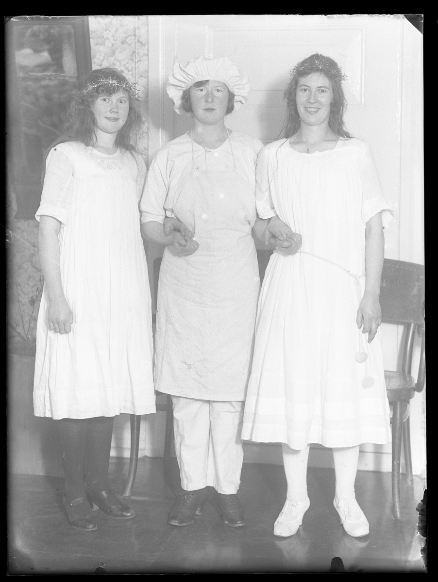 Lilly, Dagmar och Lisa fotograferade arm i arm. Alla tre bär vitt och flickan i mitten är klädd som en bagare eller kock, de andra två har kransar i håret.
