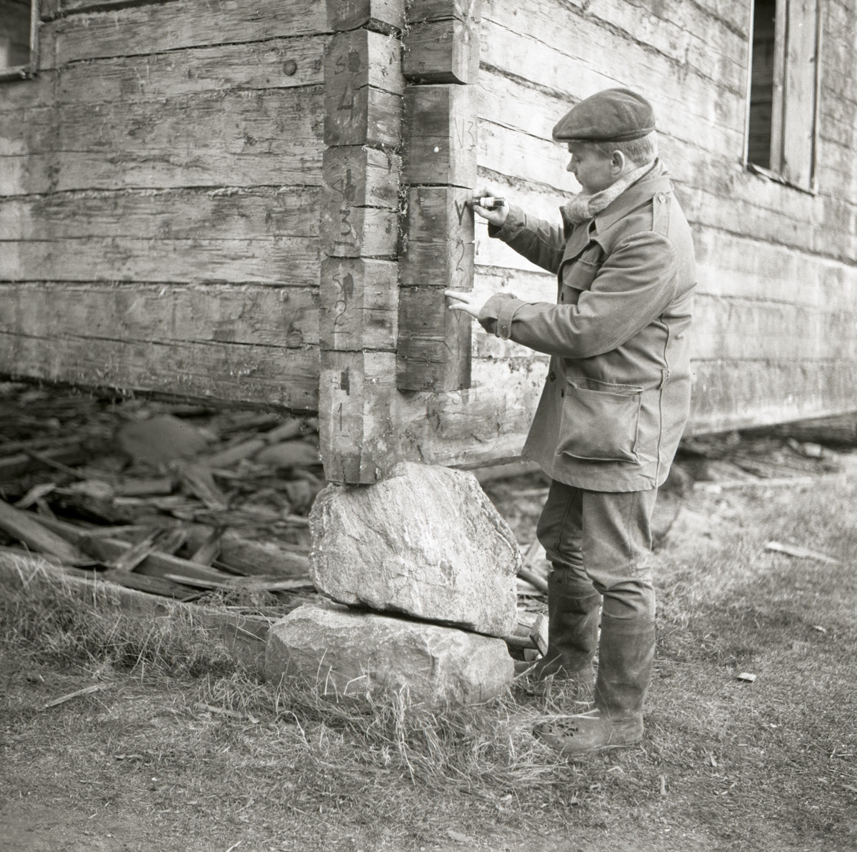 En man märker upp timmerstockar på en timrad husknut inför en flytt av byggnaden, 1967 i Rengsjö.