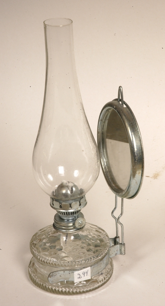 Lampa er grå, og har klart glass i beholderen som er til parafin. Påskrudd vekeholder m/ skrue til veke av bomull (hvit og blå). Pæreformet lampeglass festet i vekeholderen. Stativ m/ rundt speil festet rundt glassbeholderen.