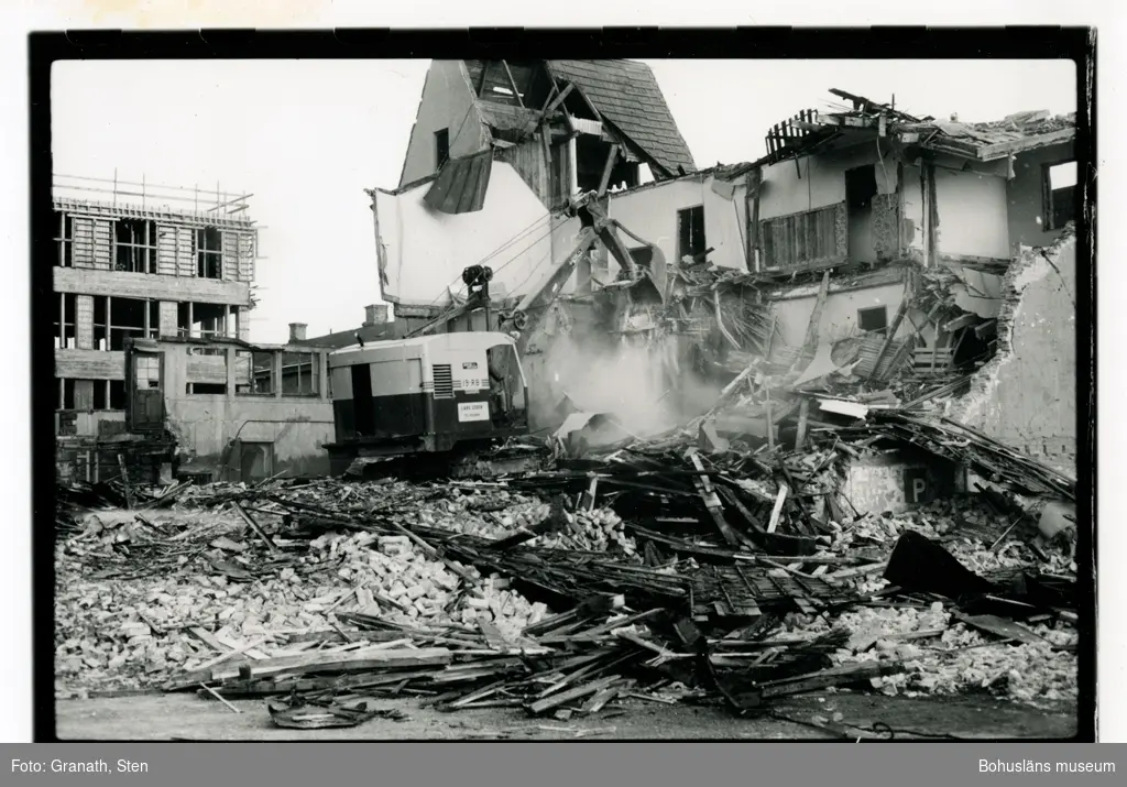 Rivning av stadshotellet på Kungsgatan. En grävmaskin i mitten av bilden river sönder ett flervåningshus. Till vänster står ett hus under uppförande där senare Nordbanken hade sitt kontor.