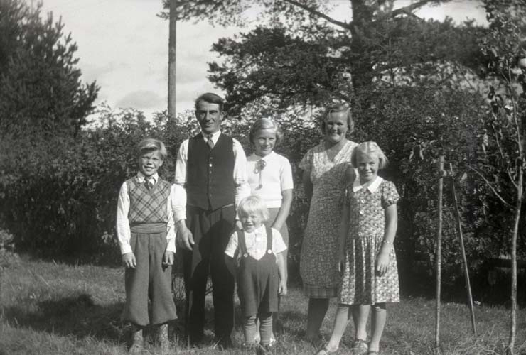 En familj bestående av far, mor och fyra barn i olika åldrar poserar i en trädgård, 1936.