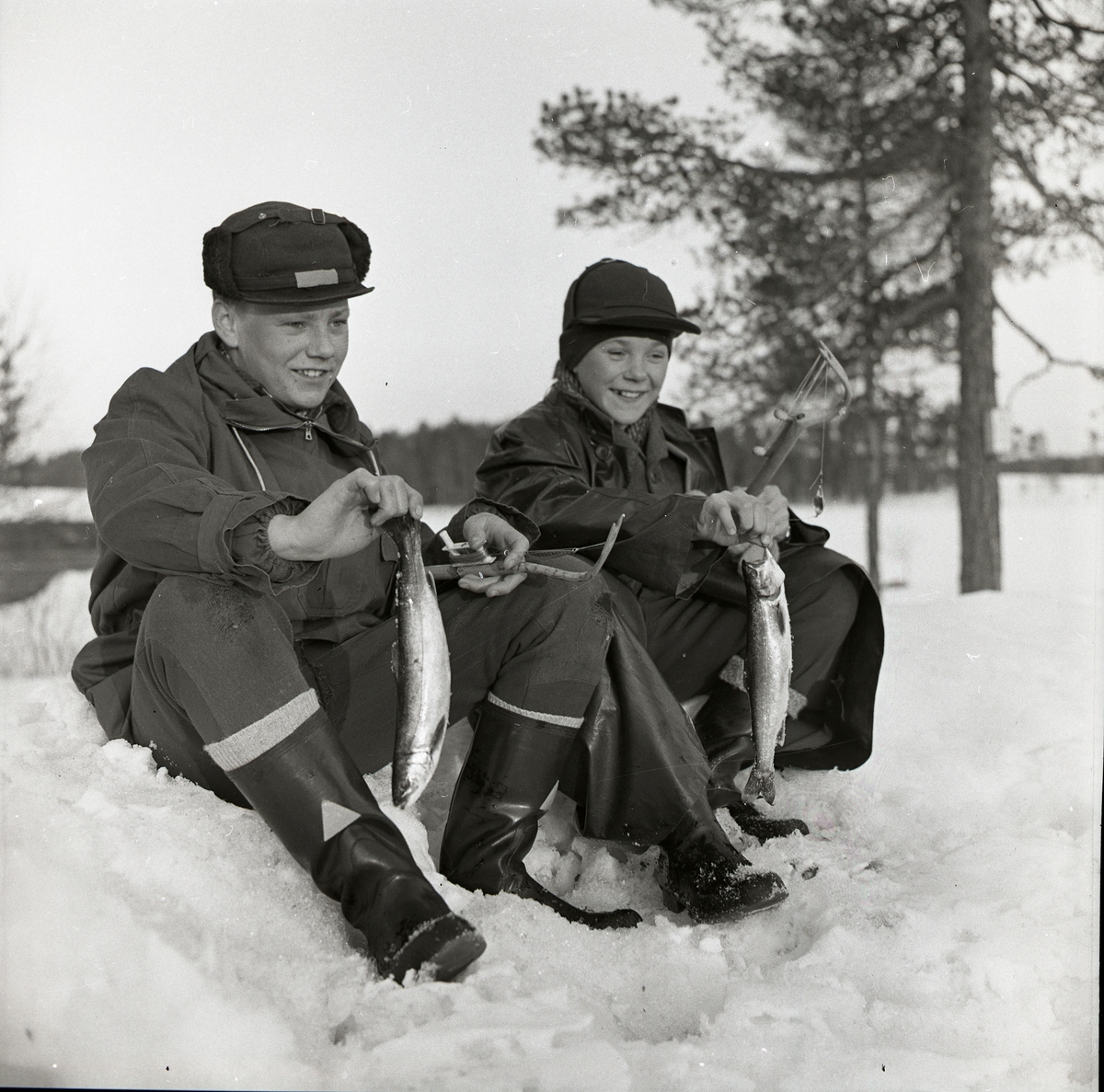 Två pojkar sitter i snö på is med varsin fisk och ett pimpelspö i händerna, Hälsen 4 maj 1958.