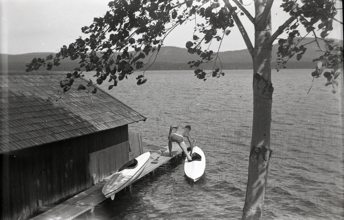 Sjö med båthus och brygga. Hilding stiger ner i en kanot, Hölesjön 1946.