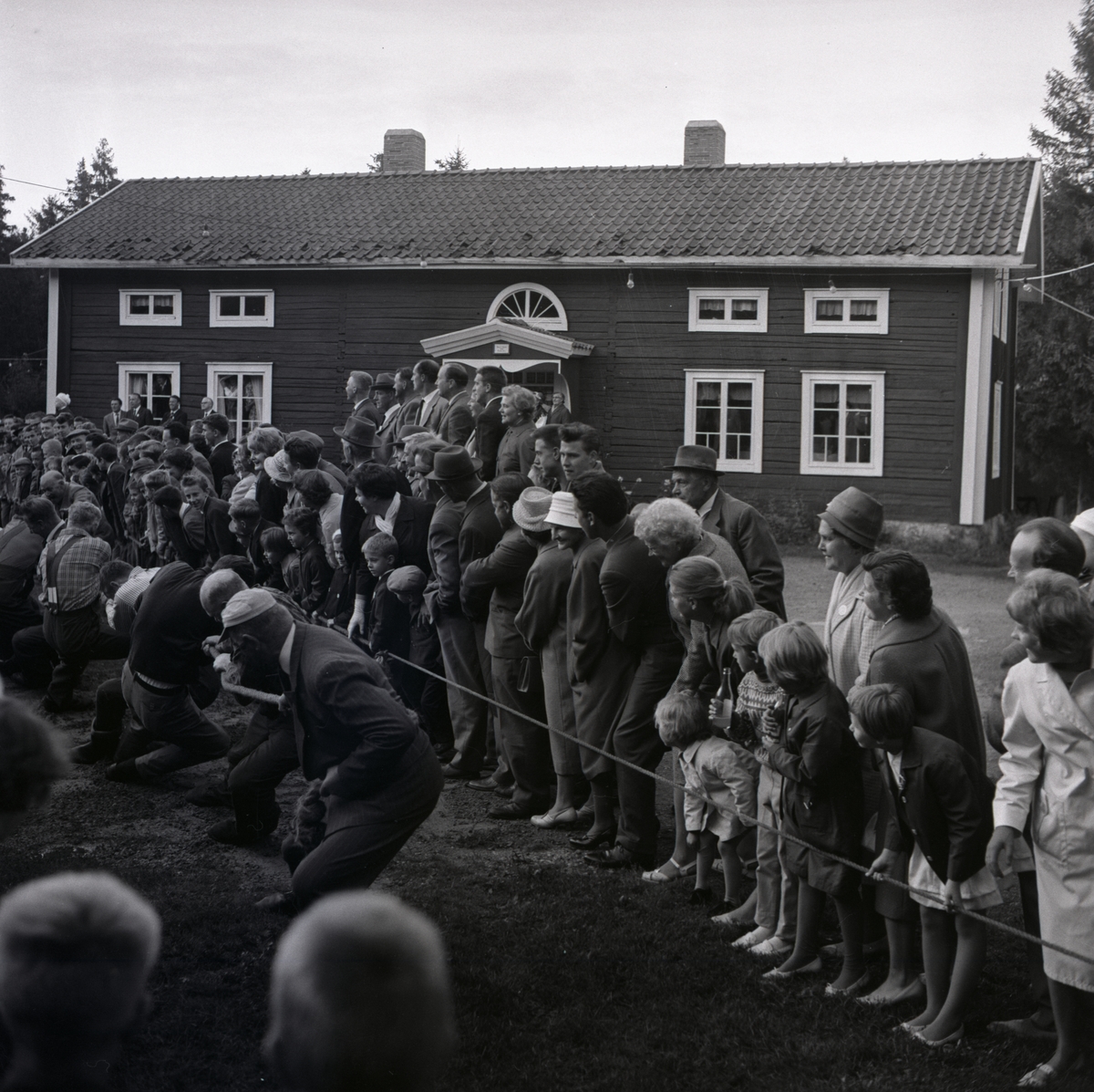 Intill Gnarps hembygdsgården pågår det en dragkamp. En grupp människor hejar på, 1950- talet i Gnarp.
