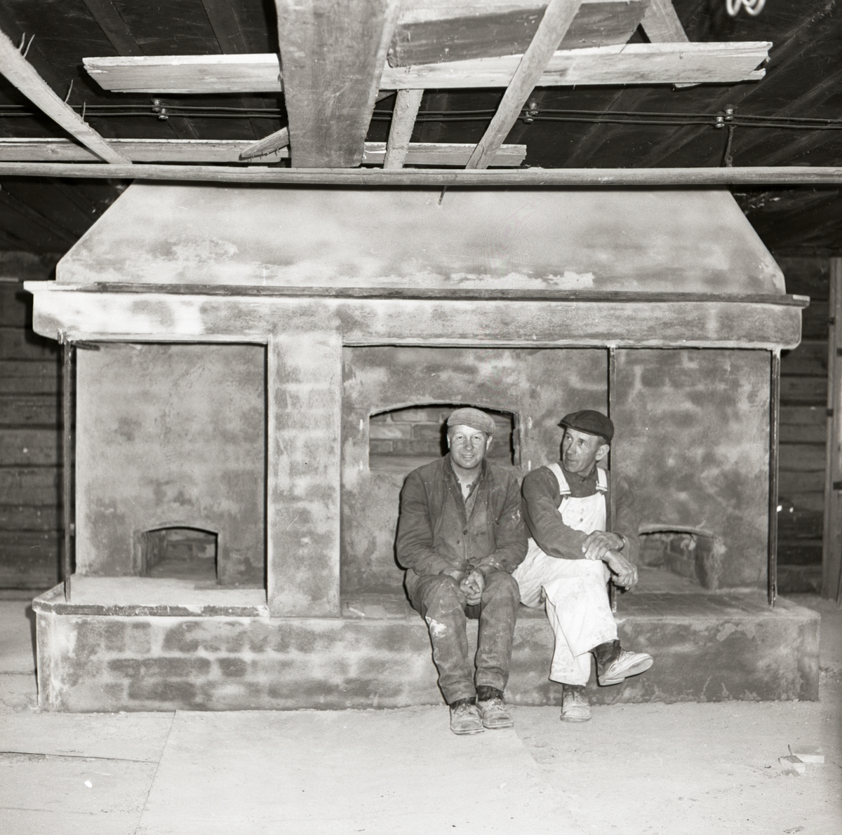 Två murare sitter på en bakugn som de har byggt i Rengsjö hembygdsgård, maj 1965.