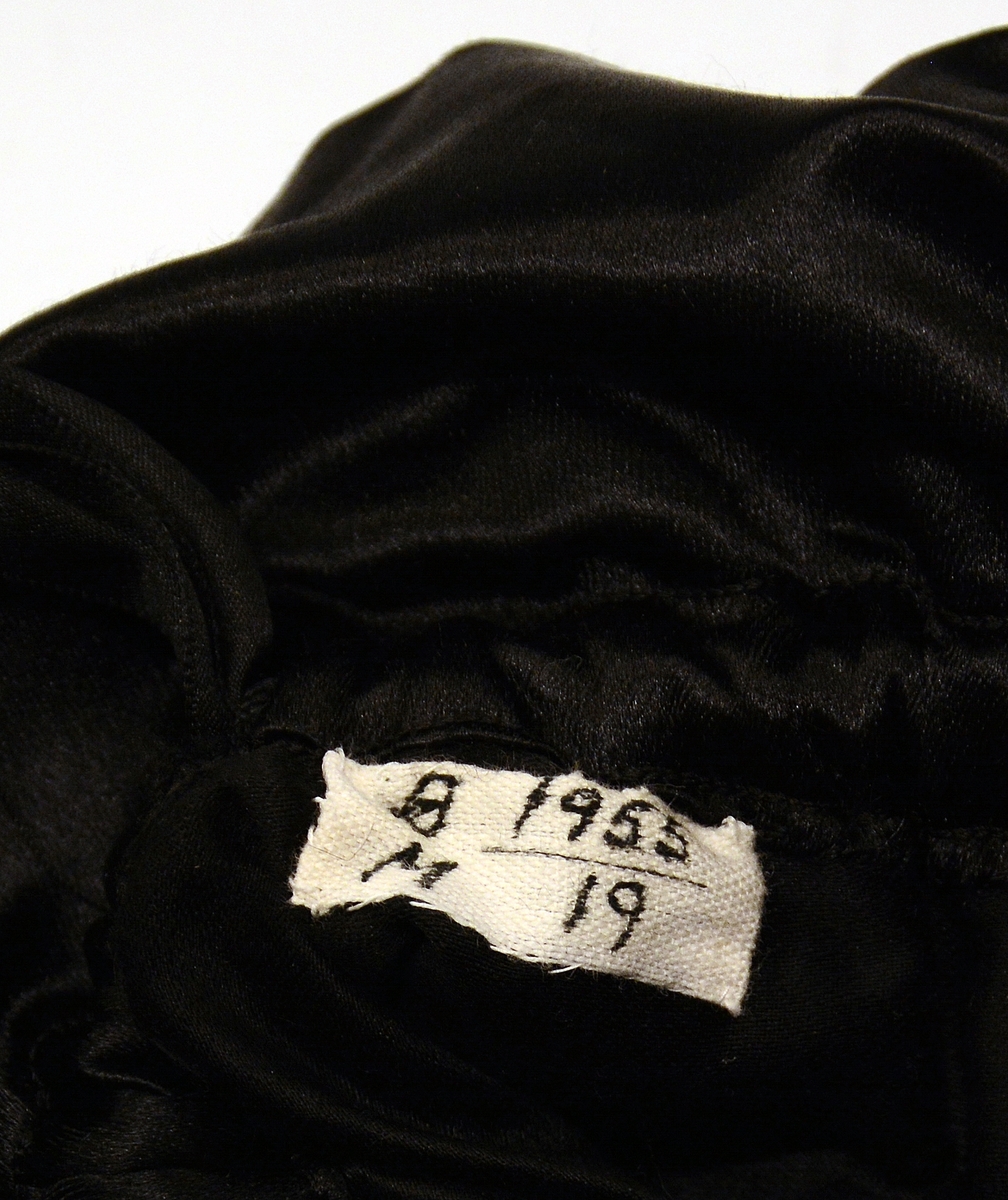 Sypose av silke med perlebroderi. Sort silke med sorte silkebånd og initialene H.K.S. (Hedvig Katharina Stousland) brodert nederst med sorte perler.
