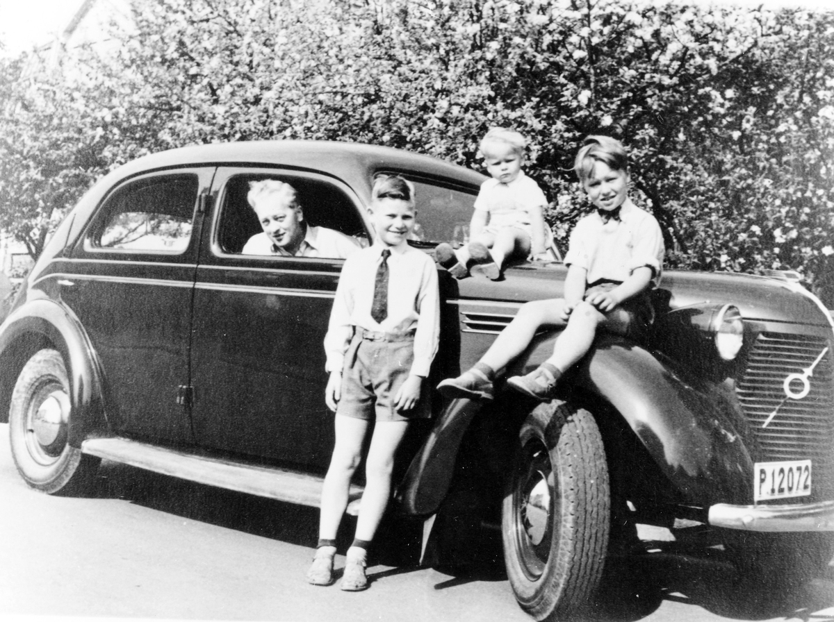 Nils Sahl sitter i sin första bil, en Volvo 1939, registreringsnummer P12072. Två av Nils söner sitter på bilen medan en lutar sig mot den. 
Bilen användes under 1950-talet.