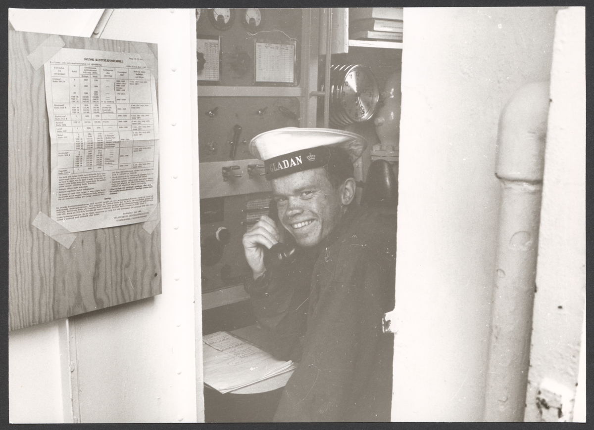 Porträtt av sjöman i radiohytten ombord på skolskeppet Gladan sommaren 1968. Mannen ler och tittar rakt in i kameran.