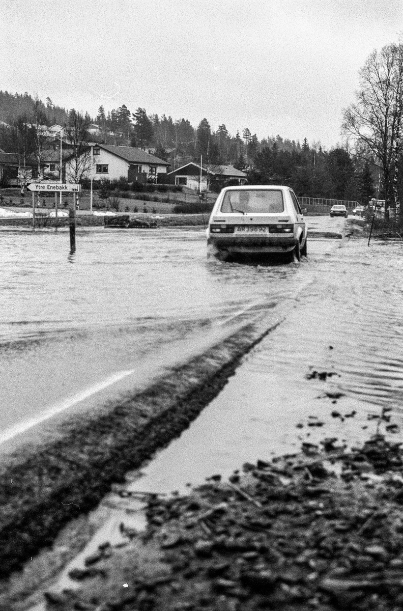 Flomskader på veiene, Riksvei 120, Ytre Enebakk. Vannet flommer over veier og jorder, biler kjører så vannspruten står.