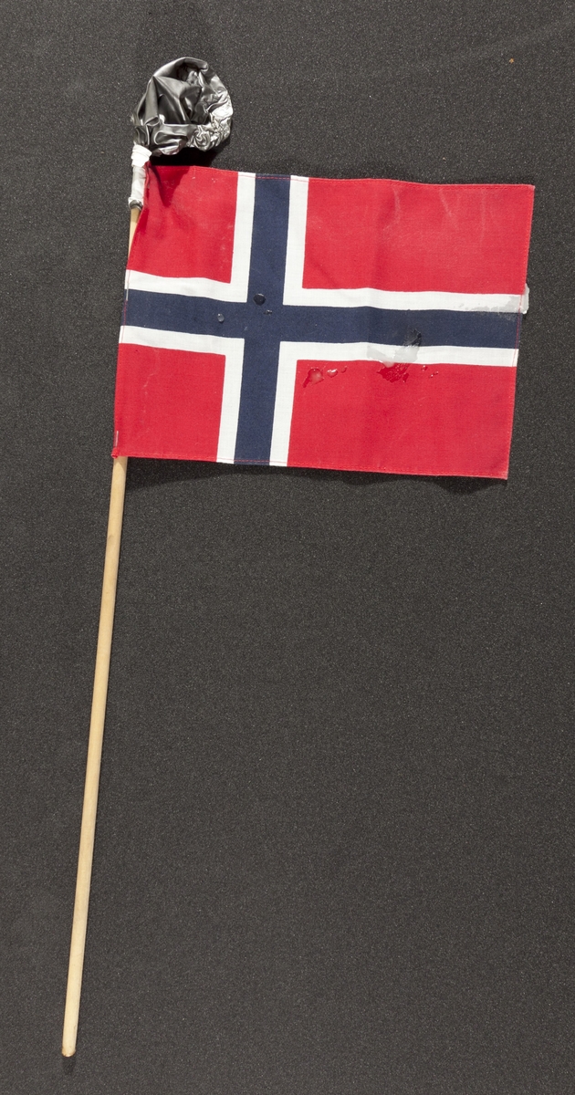 Flagg innsamlet etter terrorhandlingen 22. juli 2011 fra minnesmarkeringene i Lillestrøm. 

Klassisk norsk flagg slik vi kjenner det fra 17.mai feiringer: Blått kors i midten, hvitt kors som "omkranser" det blå (litt tynnere fargefelt) på en rød bakgrunn, de blå og hvite korset går helt til kanten av flagget. Dimensjonene på feltene er slik at de to røde felten mot pinnen er halvparten så store som de to ytterste røde feltene. Flagget brukes både av barn og voksne. På toppen av flaggpinnen er det festet en stålgrå ballong. Den er festet med hvit tape. Ballongen har mistet all luft og ser ut som den har vært i kontakt med varme/ild, da den delevis er tørket og sprø. Det er også sølt stearin flere steder på flagget.