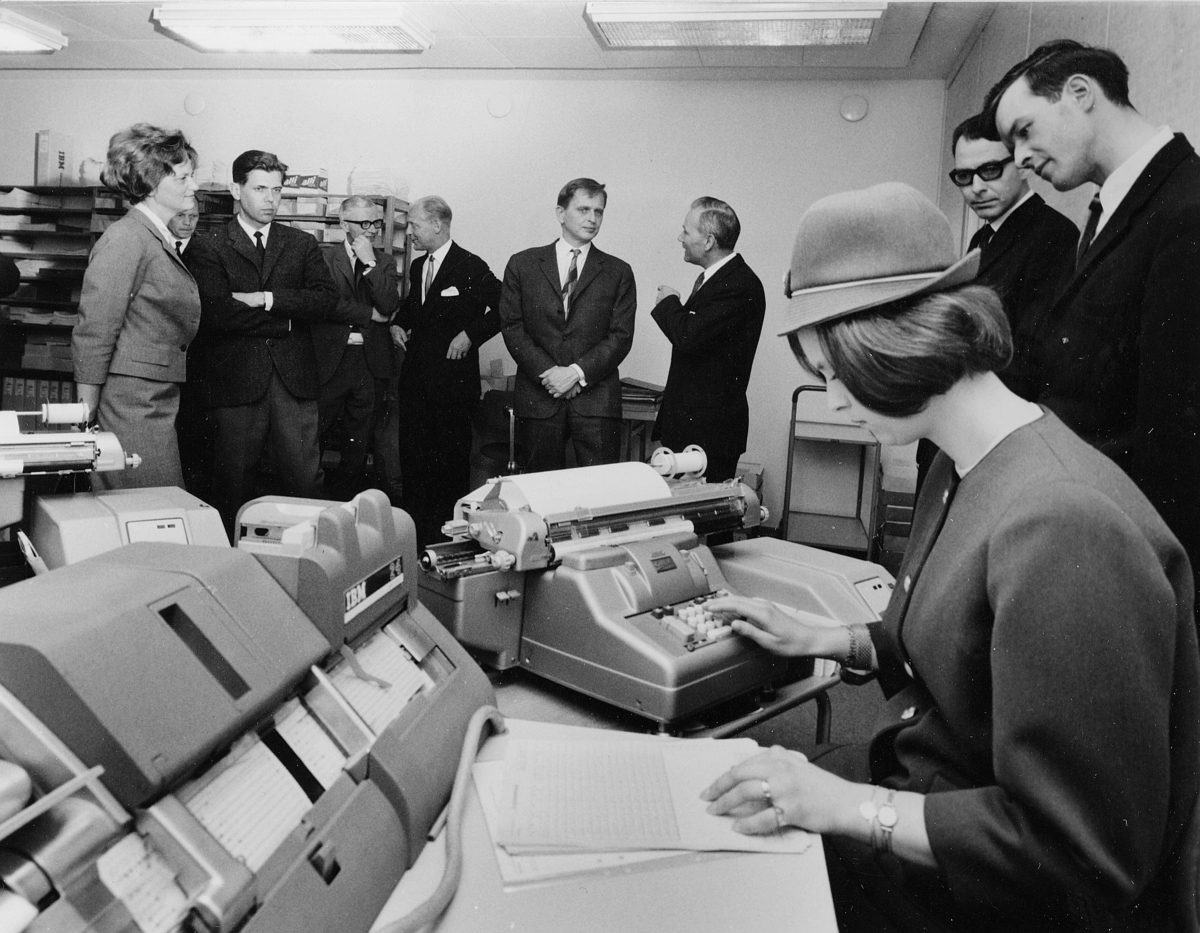 Operatrisen - för dagen klädd som postvärdinna - demonstrerar hur hennes IBM 24 (IBM Card Punch) stansar hålkort.