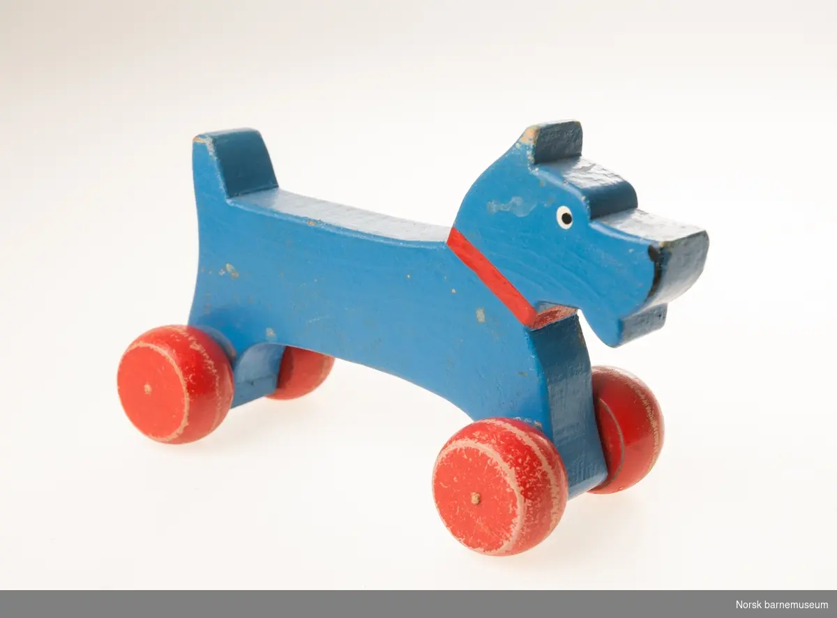 Blå lekehund i tre, på røde bevegelige trehjul.