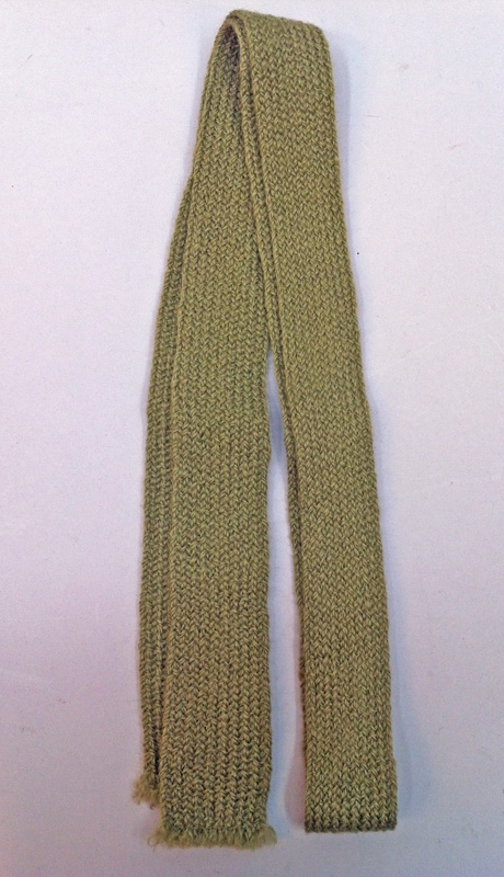 Olivgrön slips till uniform m/68, troligen maskinstickat av ull. Slipsarna är antagligen tillverkade i långa längder som man klippte av och sicksackade nertill. Det finns ingen fåll eller prydligare avslutning, heller ingen märkning av något slag.
Slipsen bars instoppad innanför jackan.