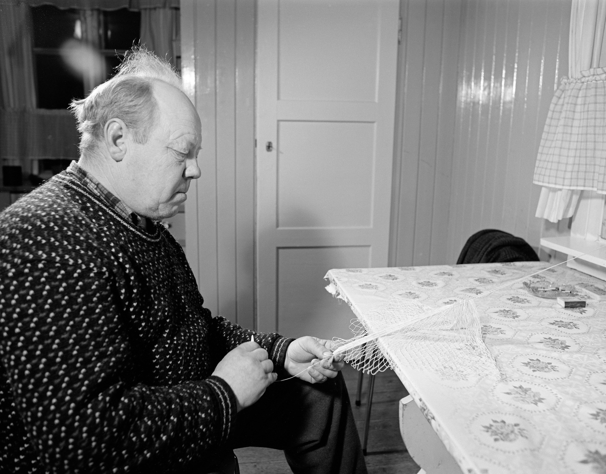 Oskar Martinussen (1921-1996) fra Fåberg binder fangstpose til en grunnhåv, såkalt «grunnhåvbunding».  Bildet er tatt på Martinussens kjøkken, der han satt ved et bord hvor plata var belagt med en mønstret voksduk, hvor det sto et askebeger med en fyrstikkeske ved siden av.  Arbeidsstykket hadde han festet i vinduskarmen framfor bordet.  Da dette fotografiet ble tatt bandt Martinussen nye masker i sona mellom bordkanten og stolen han satt på.  «Påsa'n» ble bundet av kvitt lingarn.  Redskapene Martinussen brukte var ei trenål og et «kjevle», et trestykke som gjorde det mulig å få maskene jevnstore.  På slike håver var maskevidden vanligvis 10-14 millimeter lang.  Påsa’n på grunnhåvene var oftest 80-90 centimeter lange.  De ble bundet på ovale «håvhugguer», lagd av grankvister som var bøyd sammen til en ring.  Påså’n og håvhugguet ble sammenføyd ved hjelp av lærreimer, som også beskyttet mot slitasje på bundingen når håven ble trukket langs elvebotnen.

Da dette bildet ble tatt var Martinussen kledd i en islender med ei rutete flanellskjorte under.  Kjøkkenet var faspanelt og malt med en blank, lys farge.

Grunnhåvene ble brukt under fisket etter gytevandrende lågåsild (Coregonus albula) i den nedre delen av Gudbrandsdalslågen.  Grunnhåvfisket foregikk fra strandsona.  Håven føres langs elvebotnen på en til drøyt to meters djup, i medstrøms retning.  Framdrifta måtte være noe raskere enn strømhastigheten, slik at påsan ble gående oppspent på motstøms side.  På den måten ble det rom for at lågåsilda kunne gå inn i fangstposen.  Når «drettet» skulle avsluttes, vred fiskerne litt på rauna, slik at åpningen vendte oppover slik at eventuell lågåsild ikke fikk mulighet til å svømme ut igjen.  Var det fisk i påsan, drog fiskerne håvhugguet mot seg for å tømme («skrulle») håven i bøtter, kasser eller sniker (bæreredskaper av flettverk).