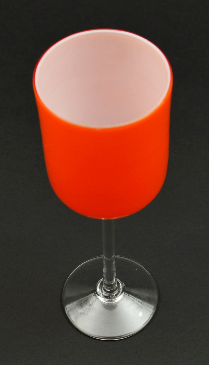 Pokal eller vase på stett.  Handblåse glas. Låg fot og nesten rett stett av fargelaust glas. Sylindrisk klokke av orange glas utanpå og opalint (kvitt) glas inni.