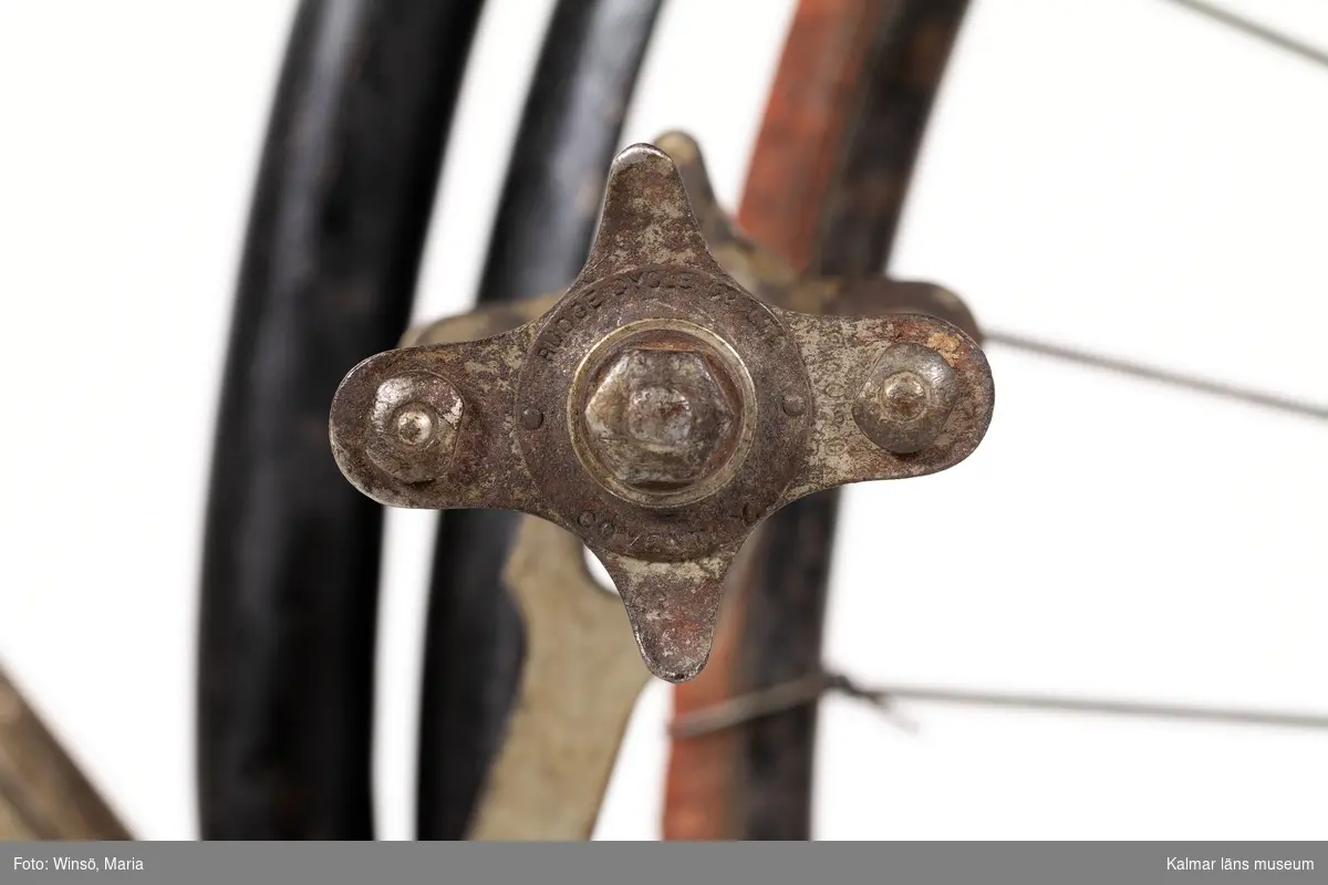 KLM 44079. Cykel. Ram av järn, hjul av stål med däck av massivt gummi och så kallat fast nav. Cykeln (velocipeden), har förstärkt korsram. Framgaffel med fjädring. Kedja med stora länkar, dvs blockkedja. Styret är höj- och sänkbart, med broms, ett äldre patent för konstruktionen, kan ha använts på en föregångare, en damcykel eller en höghjuling. Med cykelväska. Ett stort antal stämplar, bl a olika patent nr, stämpel på metallbleck på trampor: Rudge Cycle Co Ltd, Coventry. Lanserades under benämningen säkerhetscykel. Tillverkad i England, Rudge Cycle, D Rudge & Co Ltd, Coventry. Sadel, tillverkad av Brooks (vilka tillverkar sadlar än idag).