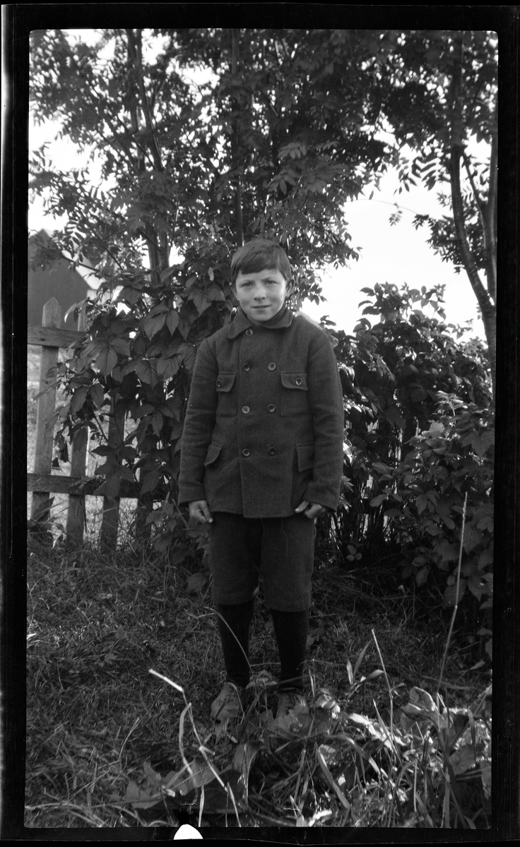 Portrett av gutt stående ved hagegjerde.