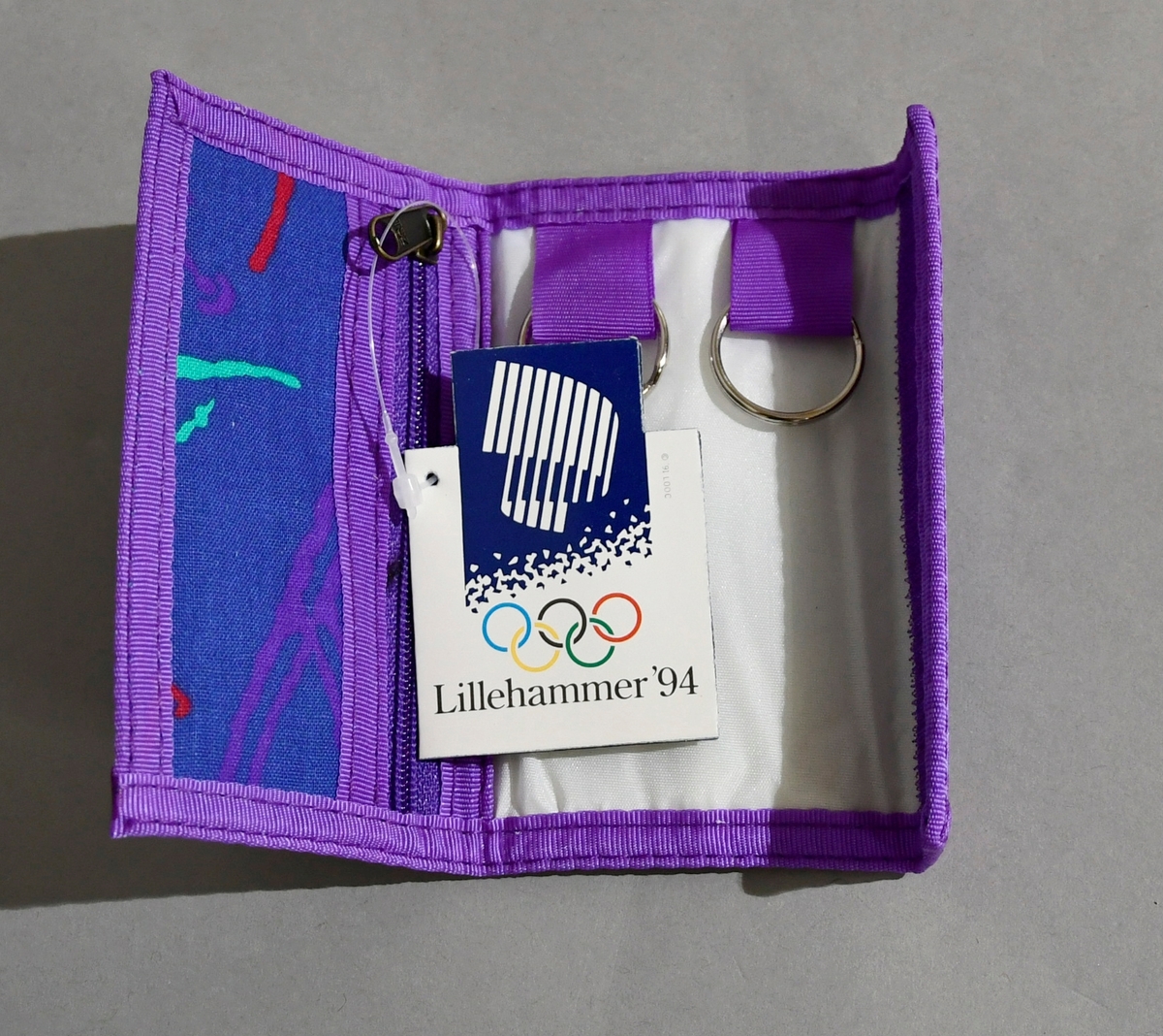 Blått nøkkelknippe med lilla kantbånd og piktogrammer i flere farger. Emblemet for Lillehammer '94 på baksiden.
