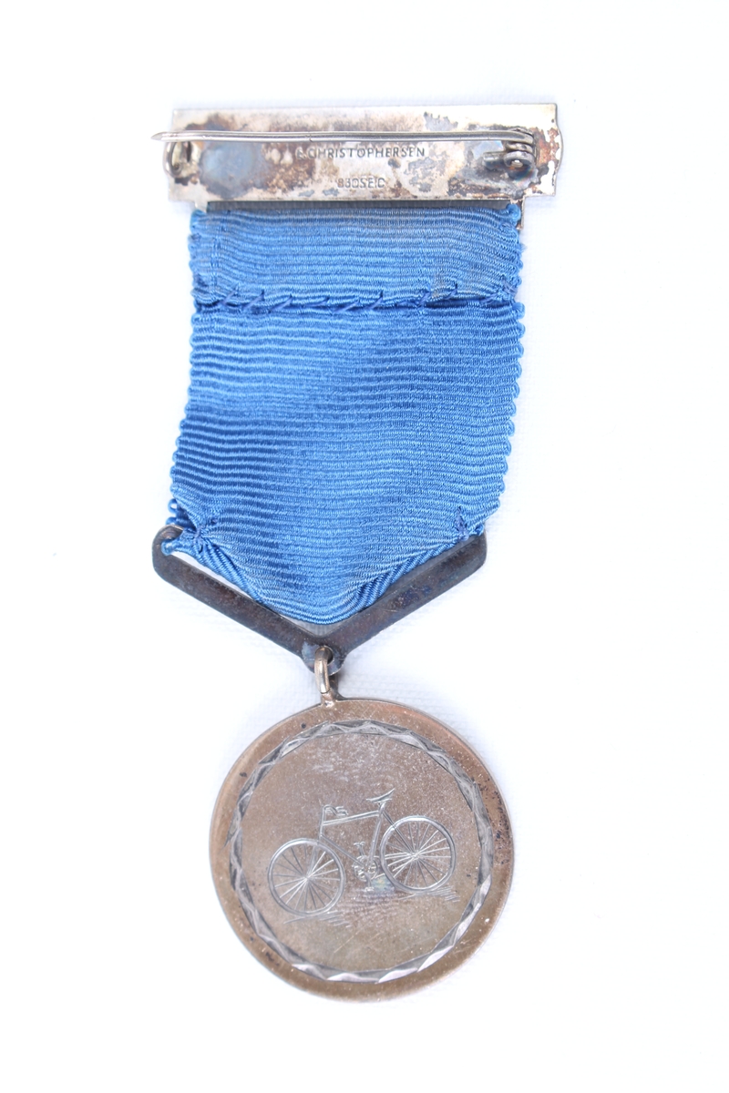 Rund medalje med blått medaljebånd og agraff.