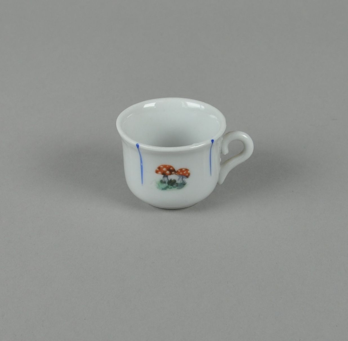 Hvit kopp av glassert keramikk, med malt dekor av nedovergående blå striper og fluesopp i midten.