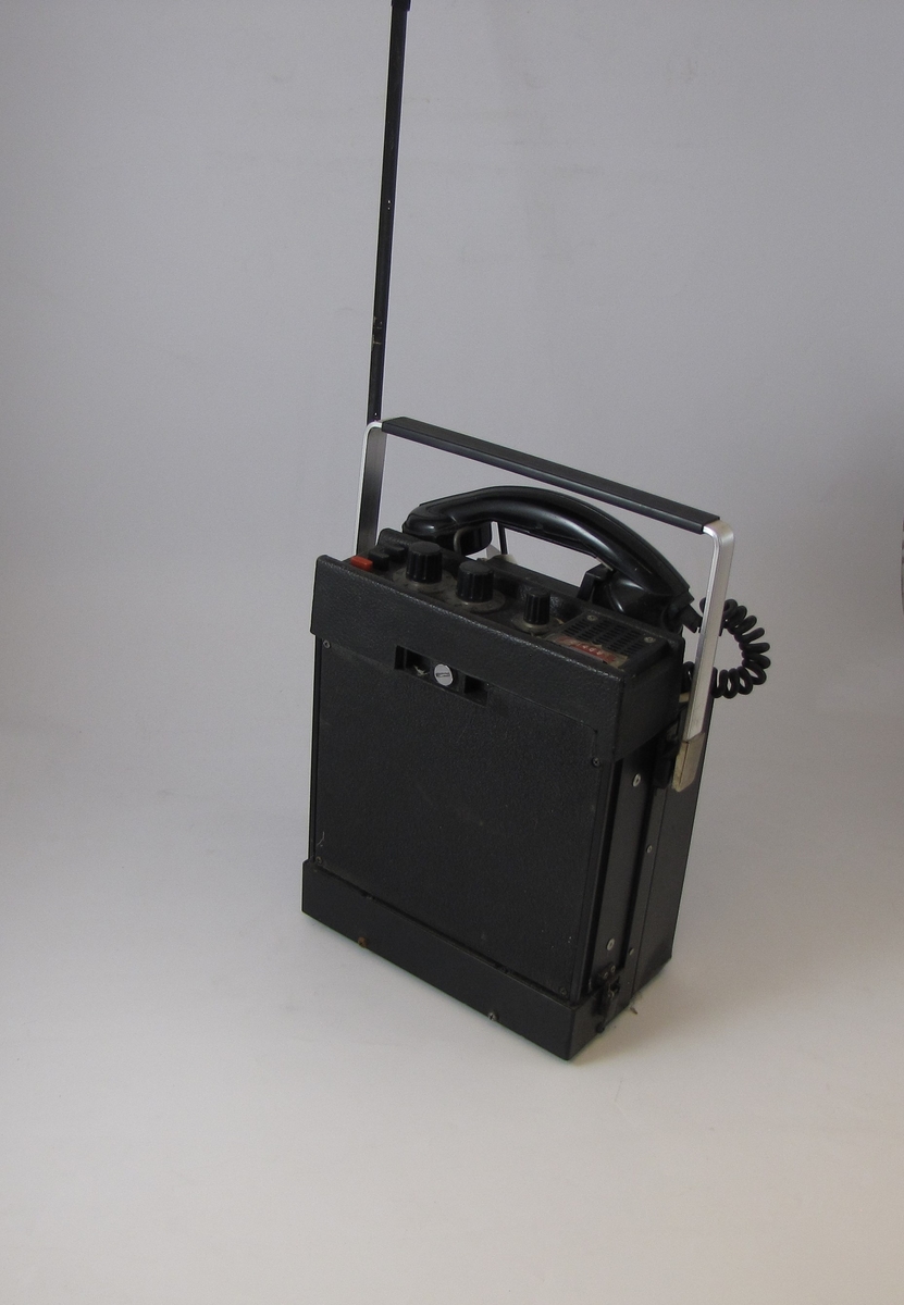 En svart rektangulær gjenstand med et håndtak, en antenne og et telefonrør. Det er tre knapper og tre vridbare knotter på en konsoll på toppen av gjenstanden, på siden av røret.