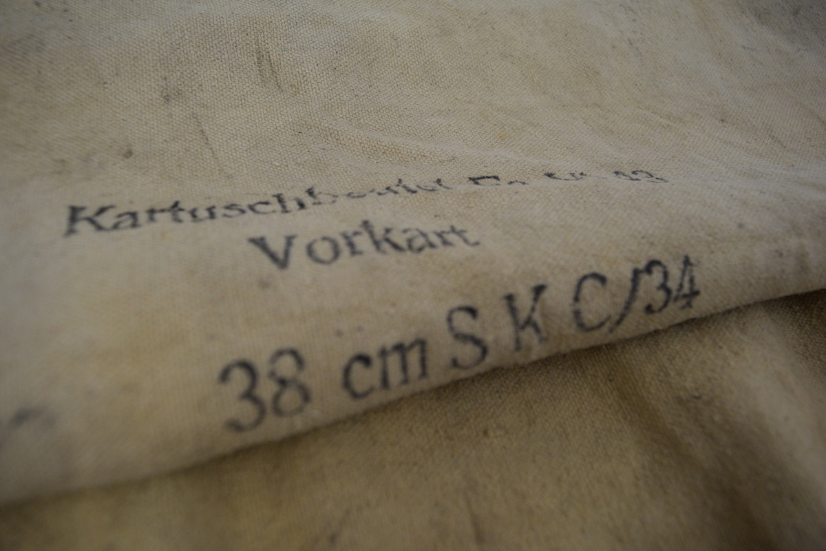 Original karduspose for drivladning tilhørende til 38 cm SK C/34 kanon på Møvig Fort. Sylindrisk form av et stykke med påsydd rundt bunn. To påsydde handtak. Håndsydde sting langs toppen.