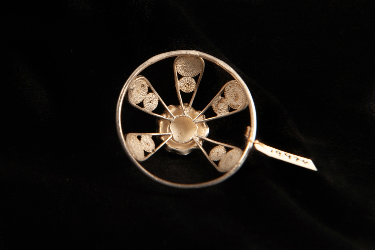 En rund malja av silver med filigranarbete, bestående av bågar upp mot en central blomma i filigran.