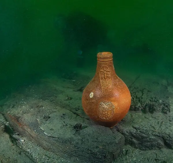 Bartmannskrukke i oransje keramikk, fra siste halvdel av 1600-tallet, står på bunnen blant båtdeler fra vraket av Pelikanen.. Foto/Photo