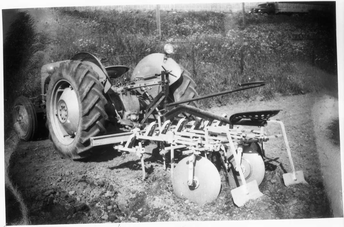 Avfotografert bilde av traktor med påmontert noe ubestemmelig redskap. Trolig er det en type radrenser for bruk i potetåker, kanskje en prototyp.