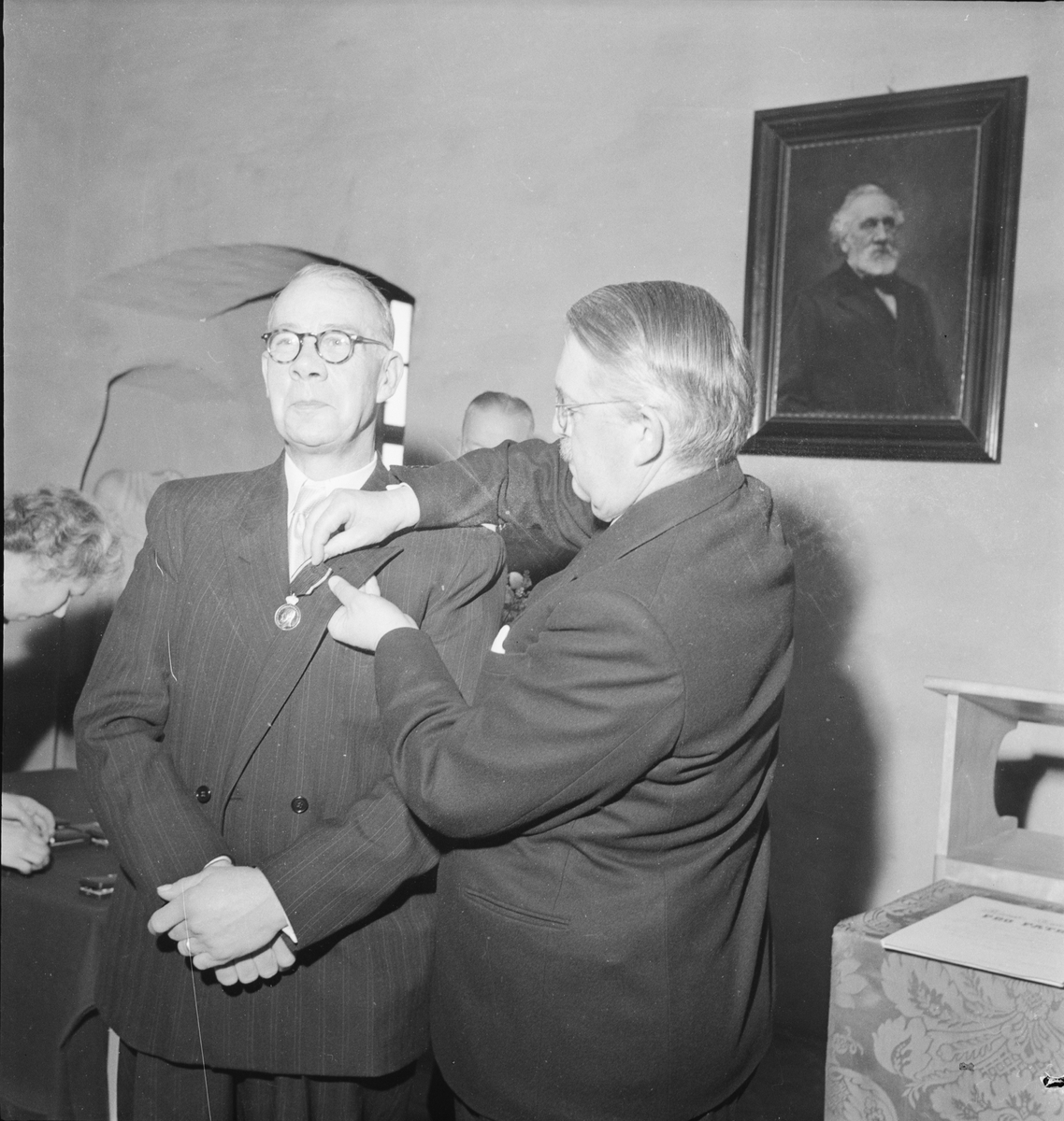 En man sätter fast en medalj på en annan mans kavajslag, 75-årsjubileum, Upsala Ångqvarns AB, Uppsala 1949