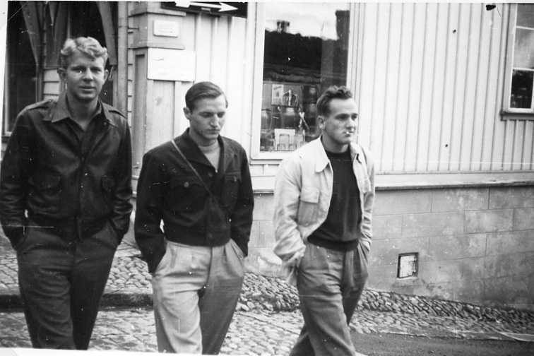 Tre unga män, L T Sanford till vänster, passerar över Ribbagårdsgränd upp vid Brahegatan. I bakgrunden syns Brahegatan 39. Mannen till höger har en cigarett i mungipan.
