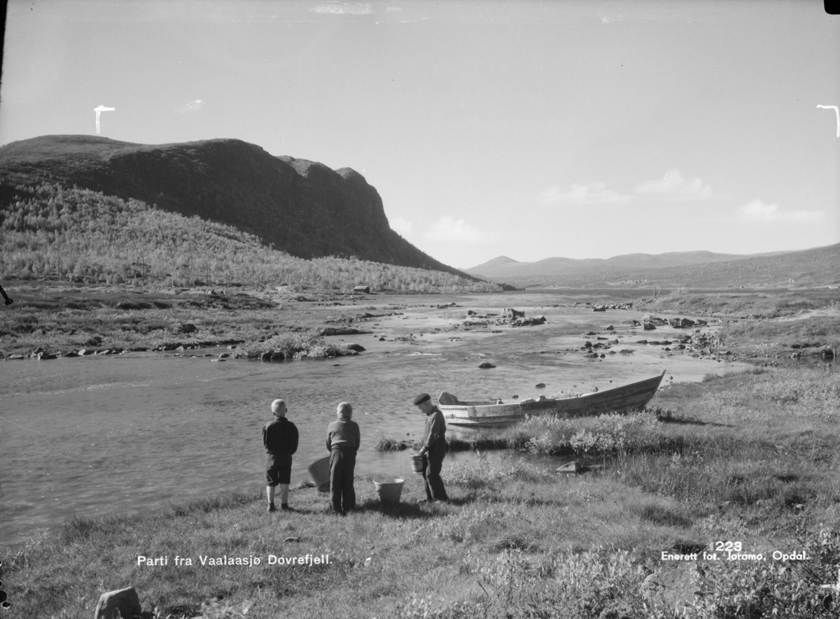 Dovrefjell, Vålåsjøen med to gutter, en mann og robå. Vålåsjøhøe bak til venstre. Påskrift: Parti fra Vaalaasjø, Dovrefjell