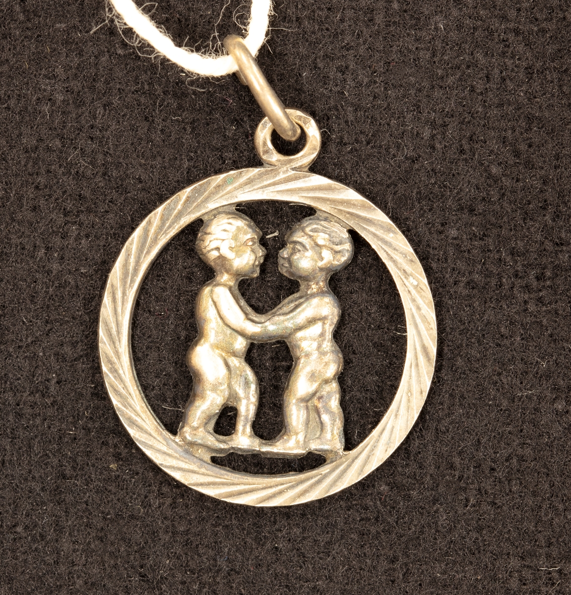 Hängberlock av silver 0,835 visande tvillingarnas stjärntecken i genombrutet mönster. Diam. 1,8 cm.

Ingår i en samling smycken som givaren köpt på auktion eller hos antikhandlare.
