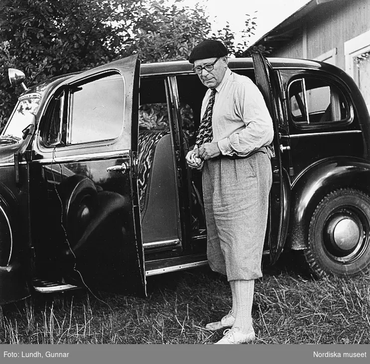 En man i basker och golfbyxor (äppelknyckarbyxor) står vid en Cadillac årsmodell 1936. bilden tagen i Skåne år 1950.