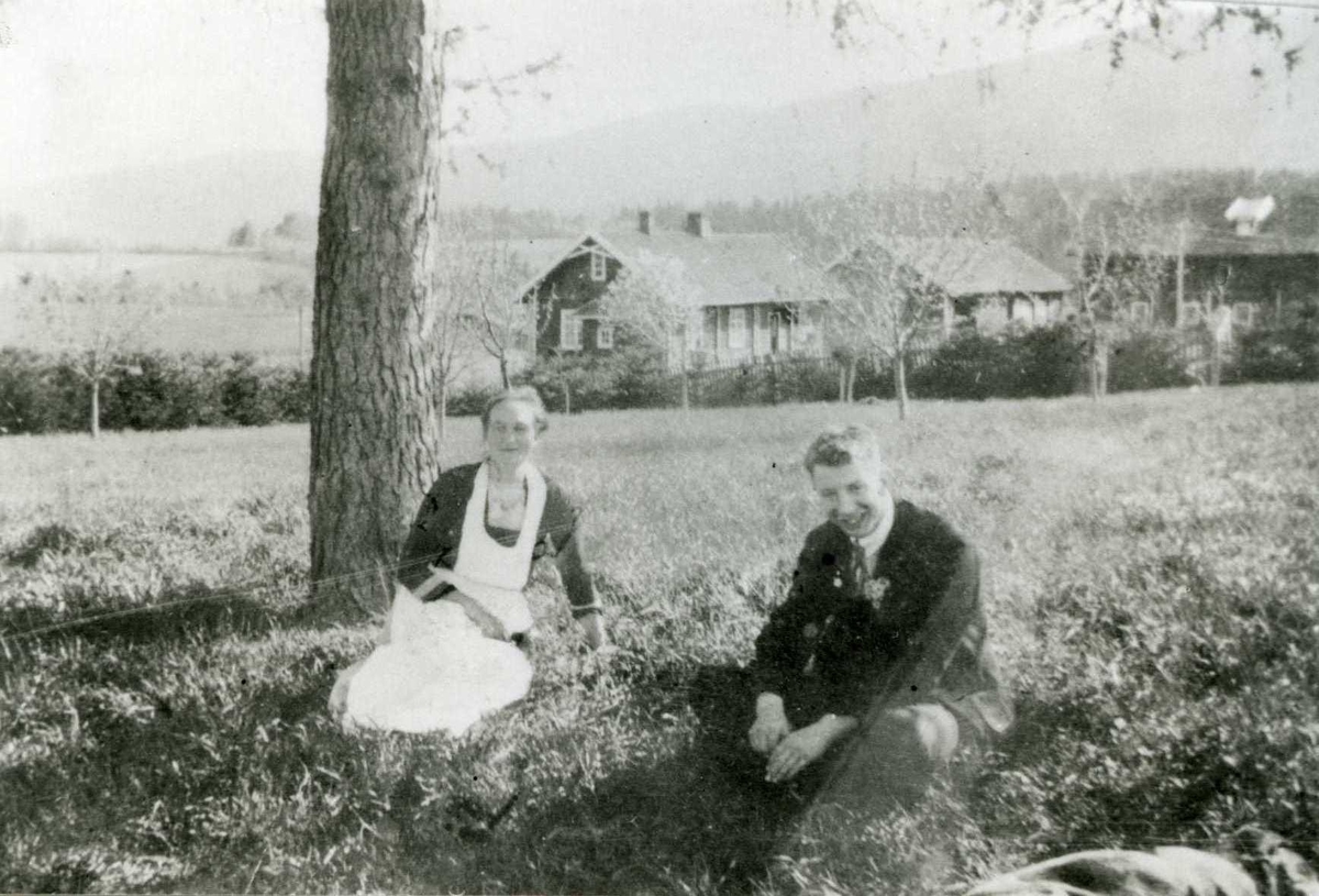 Gutt og eldre kvinne ved et tre med gården i bakgrunnen.
