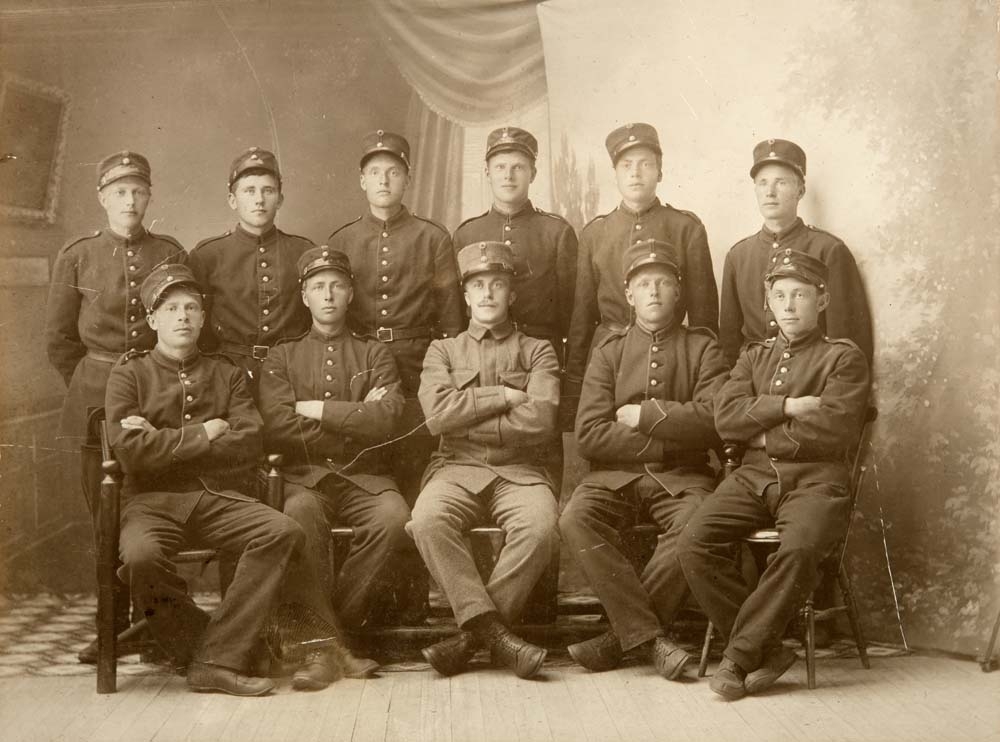 Gruppebilde med 11 soldater i uniform. Kapteinen sittende i midten. Tatt i Coldevin sitt atelier på Drevjamoen.