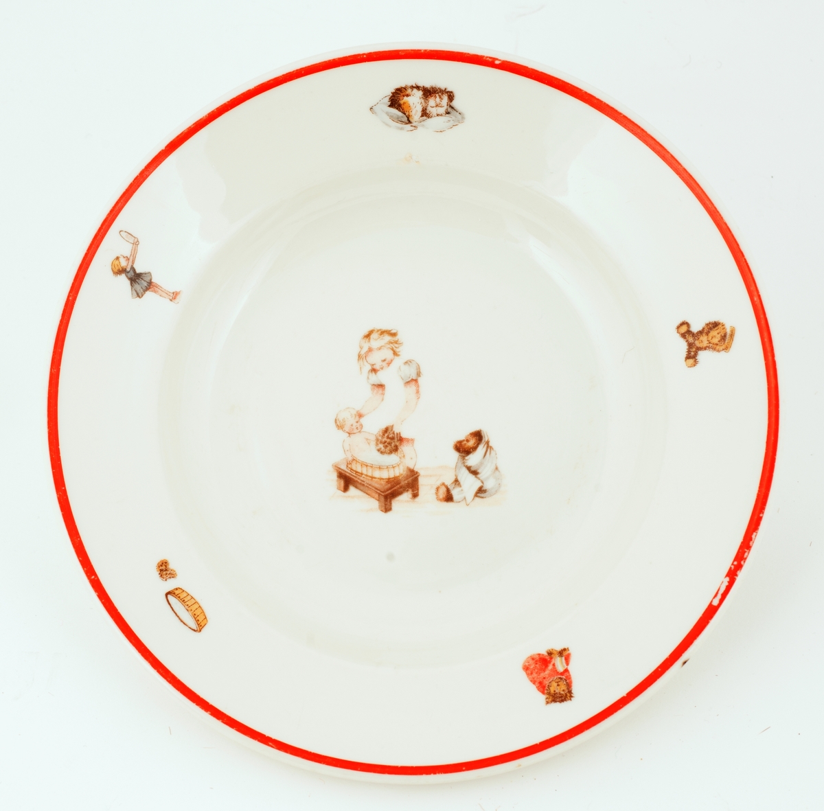 Dyp, hvit tallerken med rød munningsrand, dekorert med leketøysfigurer.