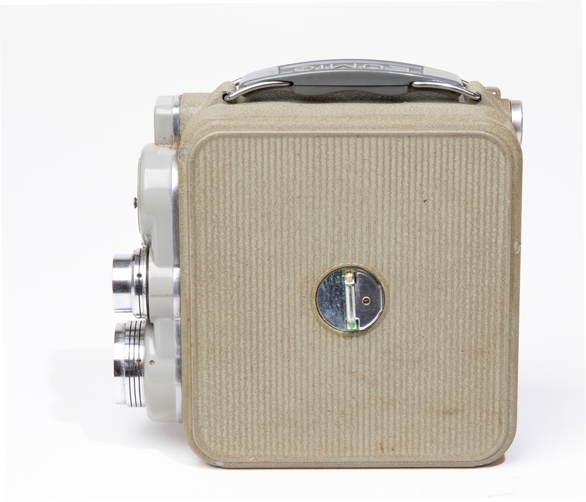 Filmkamera, dubbel-8 Eumig C 3, med kamerahus av grå metall, försedd med fjädermotor. Handtag av plast. Filmkameran är placerad i en kameraväska av brunt läder, JM 56584, och skruvas fast i väskan med en skruv. I kameraväskan förvaras ett litet linsskydd i en röd påse, och en fjärrutlösare.