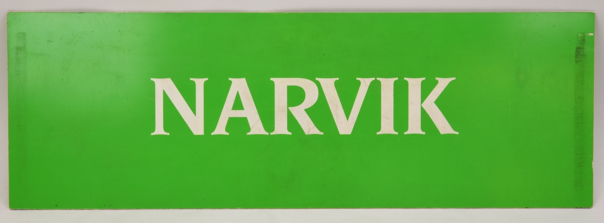 En grön avlång dubbelsidig destinationsskylt som har den vita texten "NARVIK" på båda sidor.