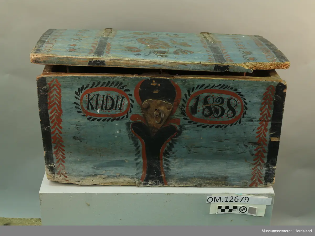 Blå rosemåla trekiste. Loket er hengsla. "KHDH 1838" er måla på framsida. Lås med nøkkel på framsida. Kista er i dårlig stand.