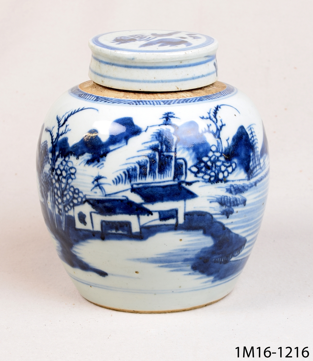 Rund urna med lock. Den är kinesisk och har vit glasyr med blå handmålad dekor föreställande bland annat ett landskap. En bojan, en burk för förvaring av ingefära.