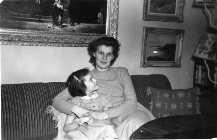 Märta Nilsson med dotter Gun sittande i soffa. Märta håller armarna om Gun som tittar upp på sin mamma. På väggen bakom dem hänger det oljemålningar.