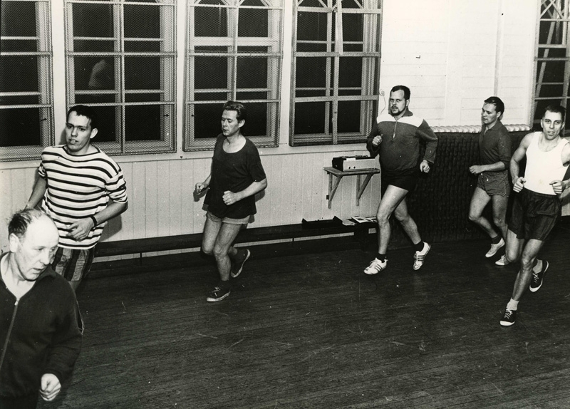 Herrar i Kållereds gymnastikförening motionerar i Stretereds gymnastiksal, 1960-tal. Ledaren Sven Olof Andersson (1924 - 2012) ses längst till höger i vit tröja.