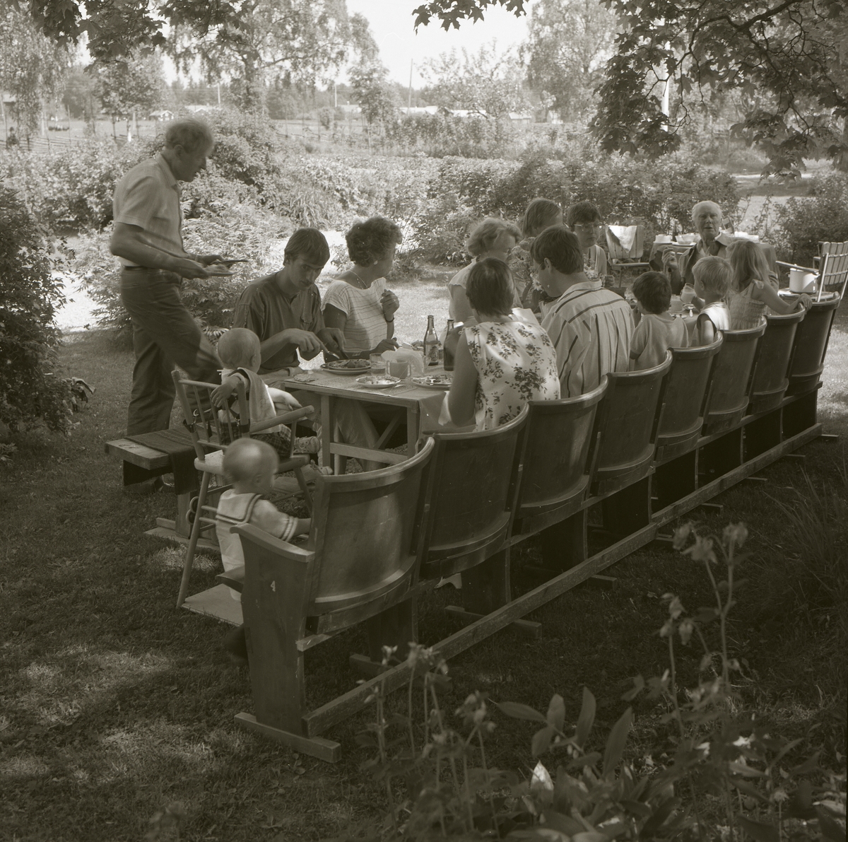 En grupp människor har satt sig till bords och äter under en midsommarfest på gården Sunnanåker, 22 juni 1985.
