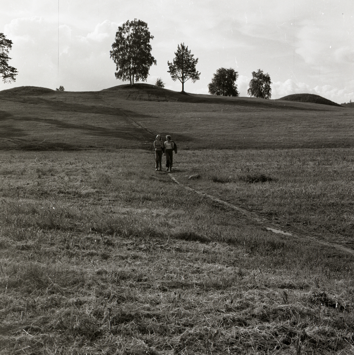 Två kvinnor vandrar på en gångstig och bakom sig har de tre stora gravhögar, Frånö, Kramfors, Ångermanland.
