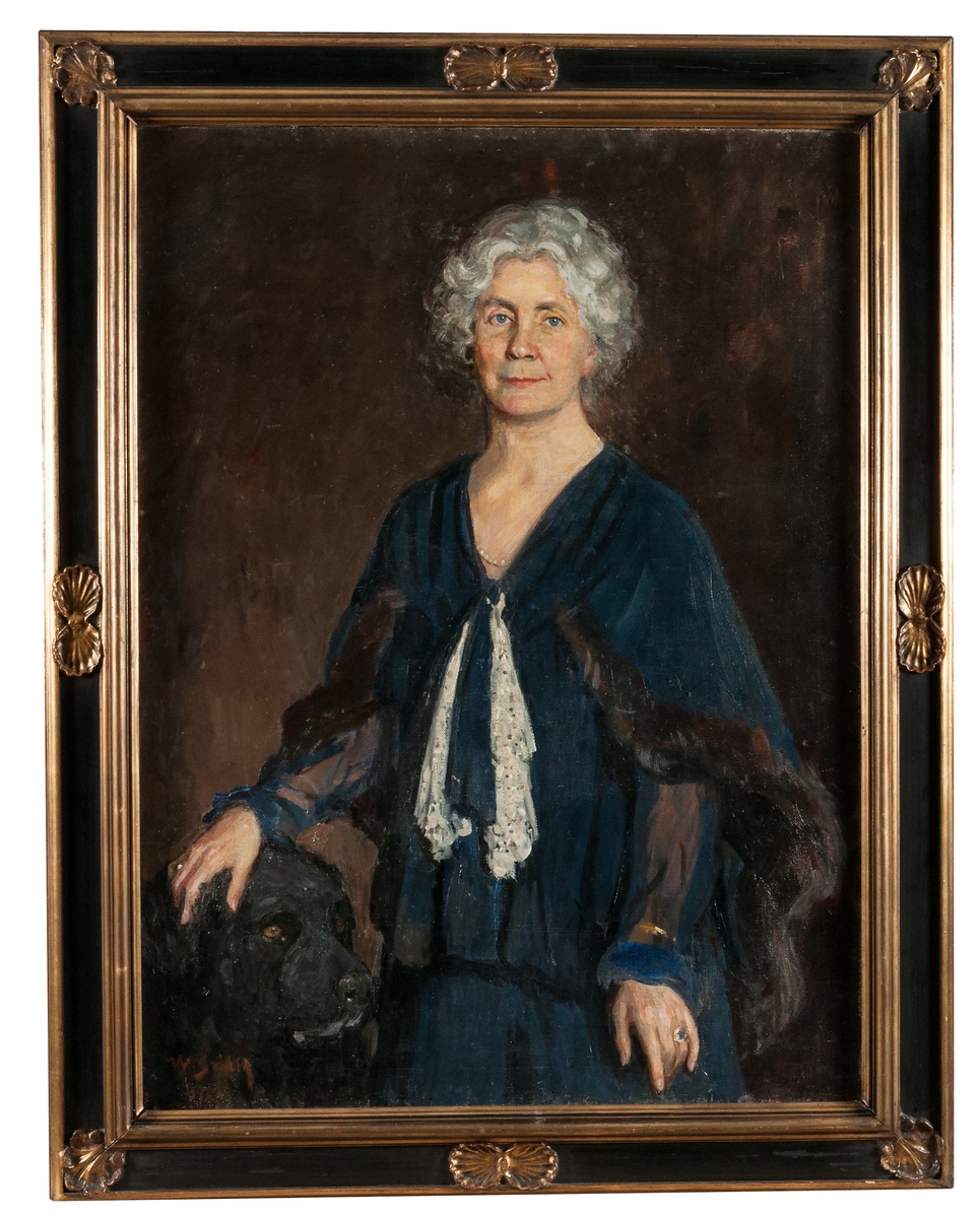 Tavla, olja på duk, svart ram med förgyllda lister och snäckor i relief. Porträtt av Hedvig Ulfsparre (1877-1963) i blå cape med pälsbräm, utfört av konstnär Wilhelm Smith 1932.