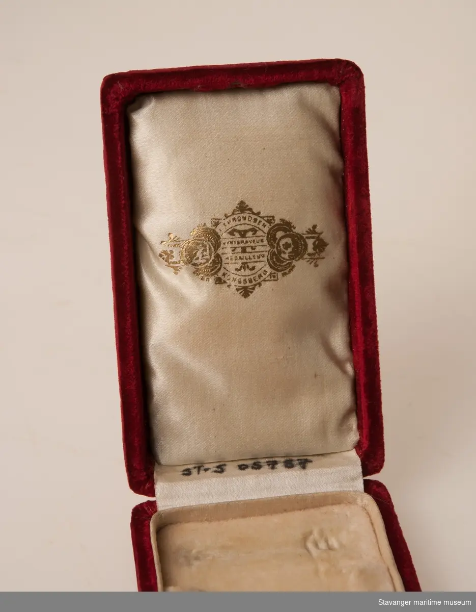 Kongens Fortjenstmedalje i gull. Medaljen er rund med kongekrone på toppen. Kong Haakons
profil er preget på medaljens forside med tekst. På baksiden en krans med tekst i midten.